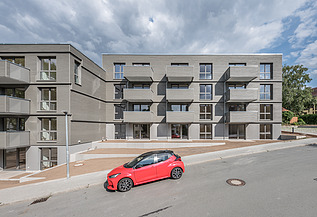 Joseph-Stiftung, Bayreuth MOLENO Foto der Joseph-Stiftung in Bayreuth. Man sieht ein Gebäude mit grauer Fassade und ein vorbeifahrendes, rotes Auto.